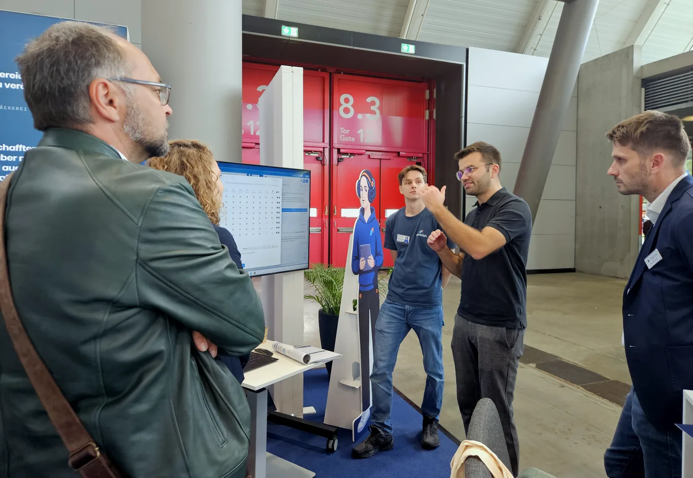 Besucherinnen und Besucher lassen sich ADA am Monitor auf dem AIPERIA-Stand der Südback 2026 zeigen